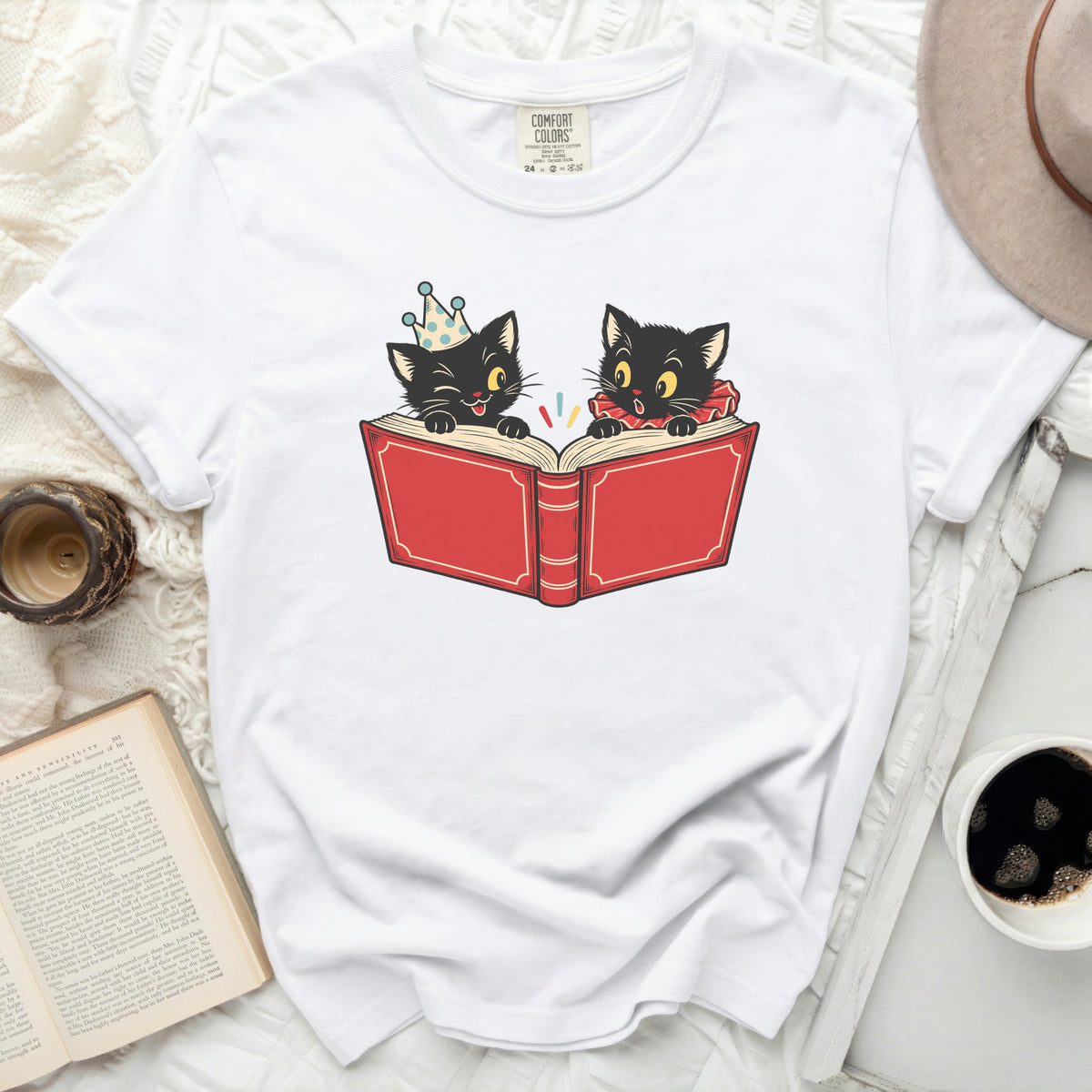 Two black cats read a red book, one wearing a party hat.