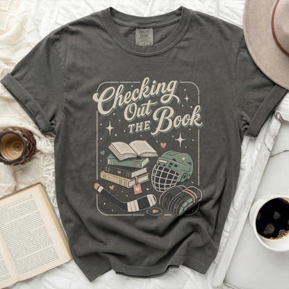 Graphic tee with "Checking The Book" text, hockey gear, and books.