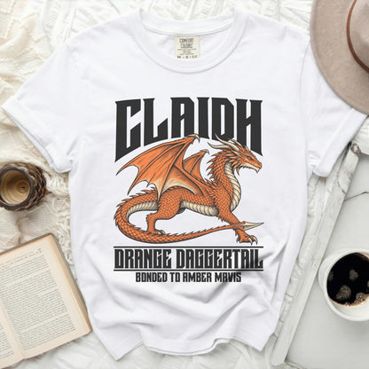 White t-shirt with an orange dragon graphic and text "CLAIDH ORANGE DAGGERTAIL BONDED TO AMBER MAVIS".