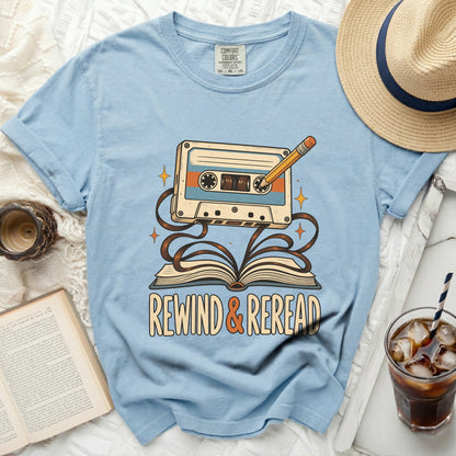 Light blue t-shirt with a cassette tape and book graphic saying "Rewind & Reread."