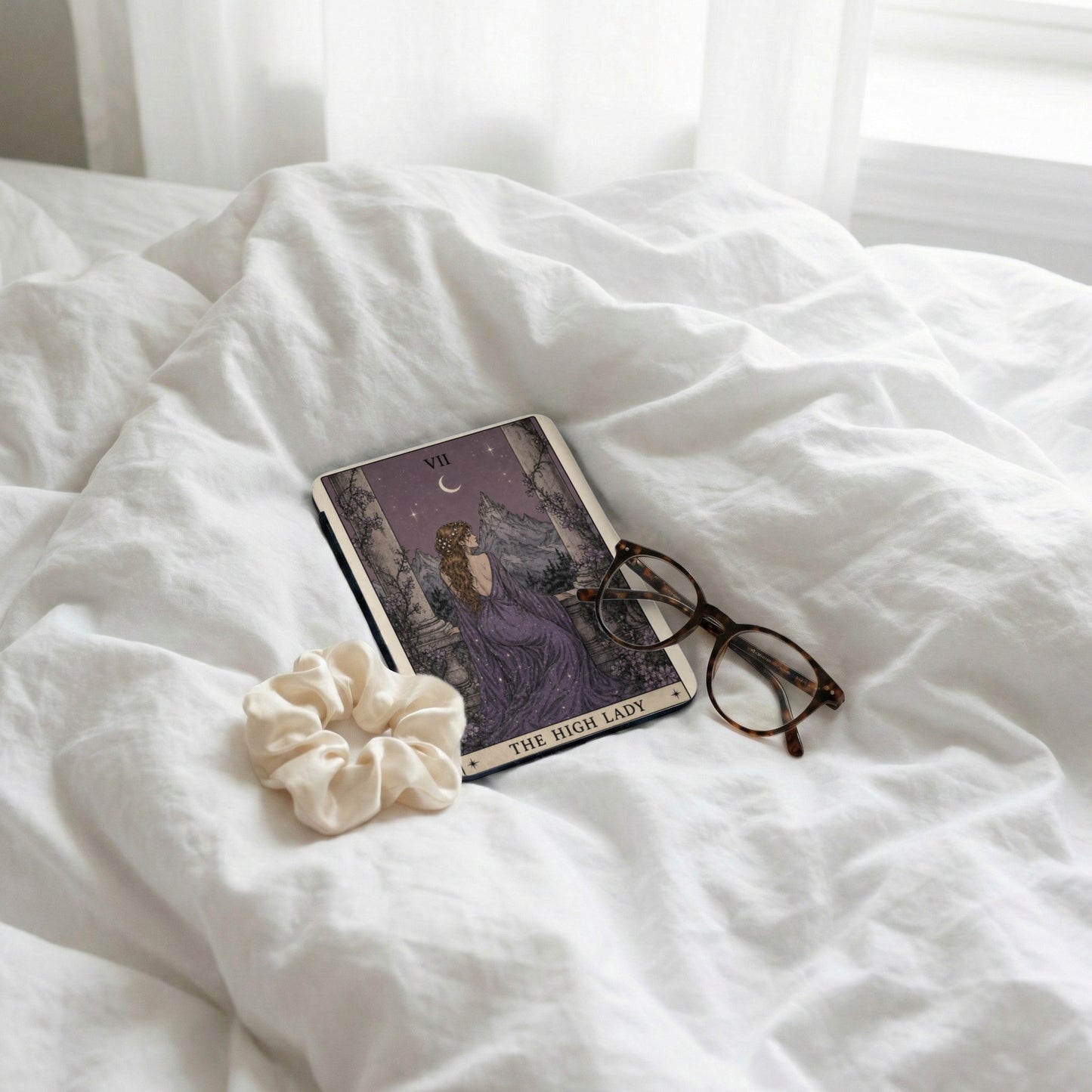Tarot card "The High Lady" with glasses and scrunchie on wrinkled white sheets.