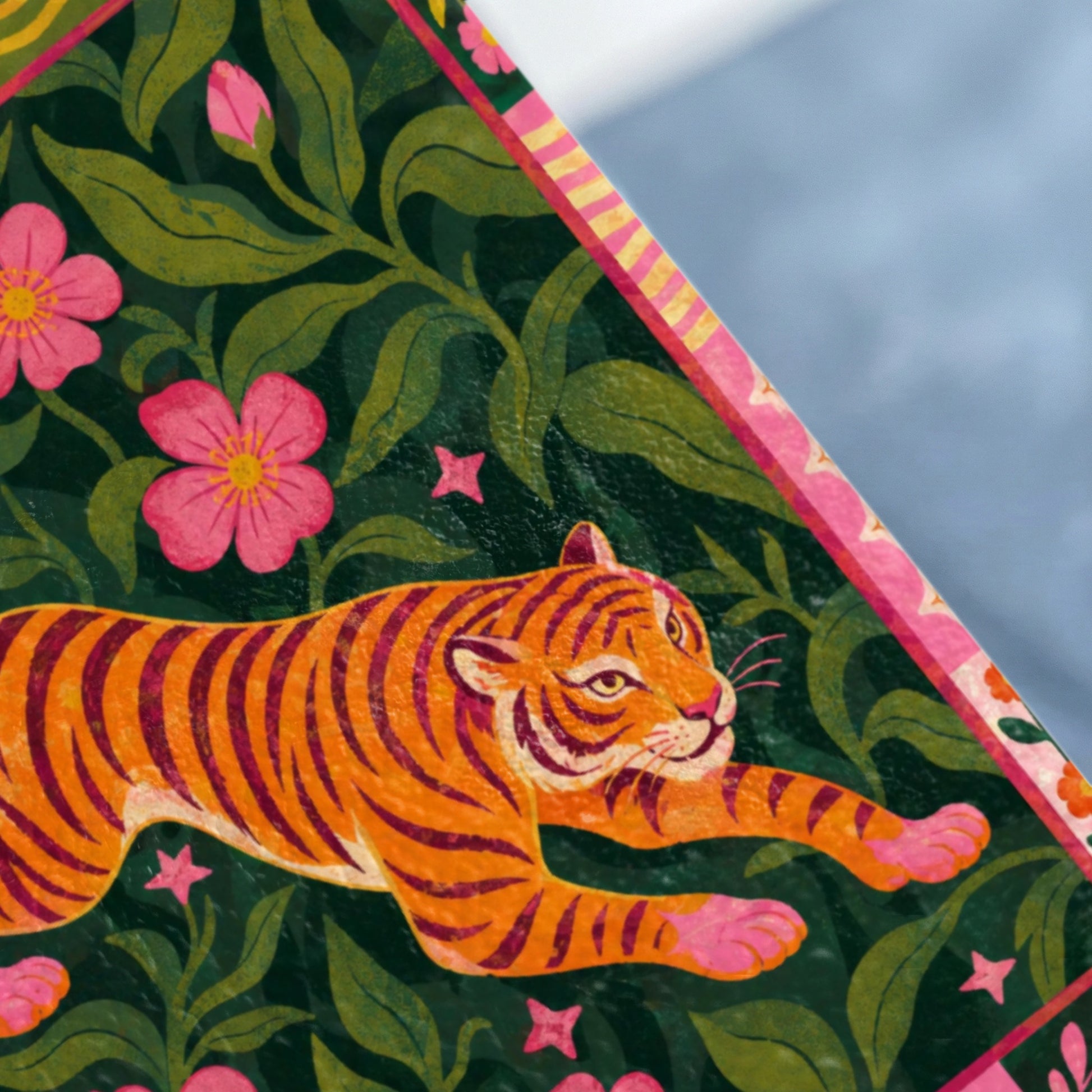 Orange tiger with pink flowers and green foliage on a patterned surface.