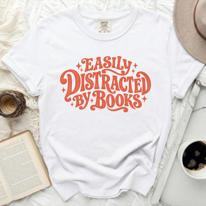 White t-shirt with orange text that reads "Easily Distracted By Books".