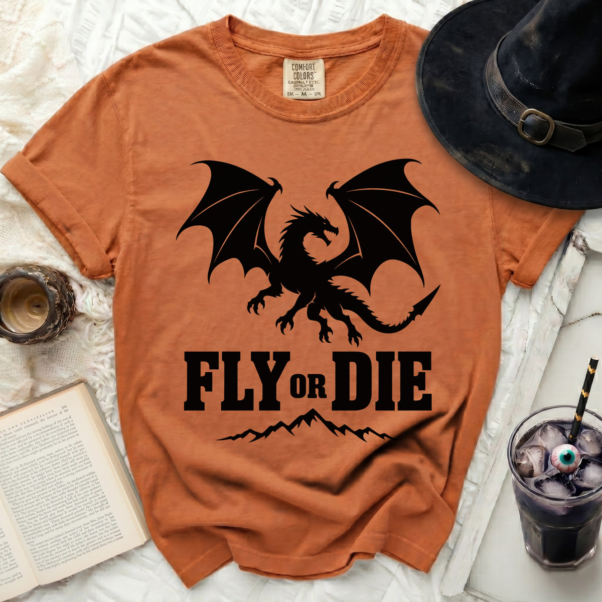 Rust-colored t-shirt featuring a black dragon graphic, the text "FLY OR DIE," and mountain silhouettes.