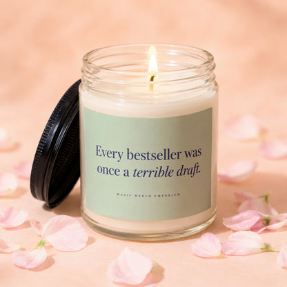 Glass jar candle with lit wick and label reading "Every bestseller was once a terrible draft."