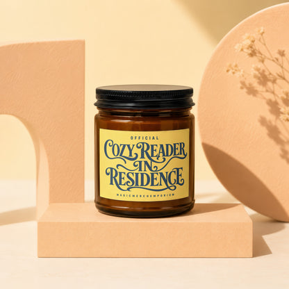 Candle with "Official Cozy Reader In Residence" text on yellow label.