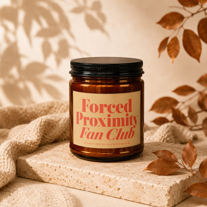 Amber jar candle with "Forced Proximity Fan Club" label and autumn leaves.