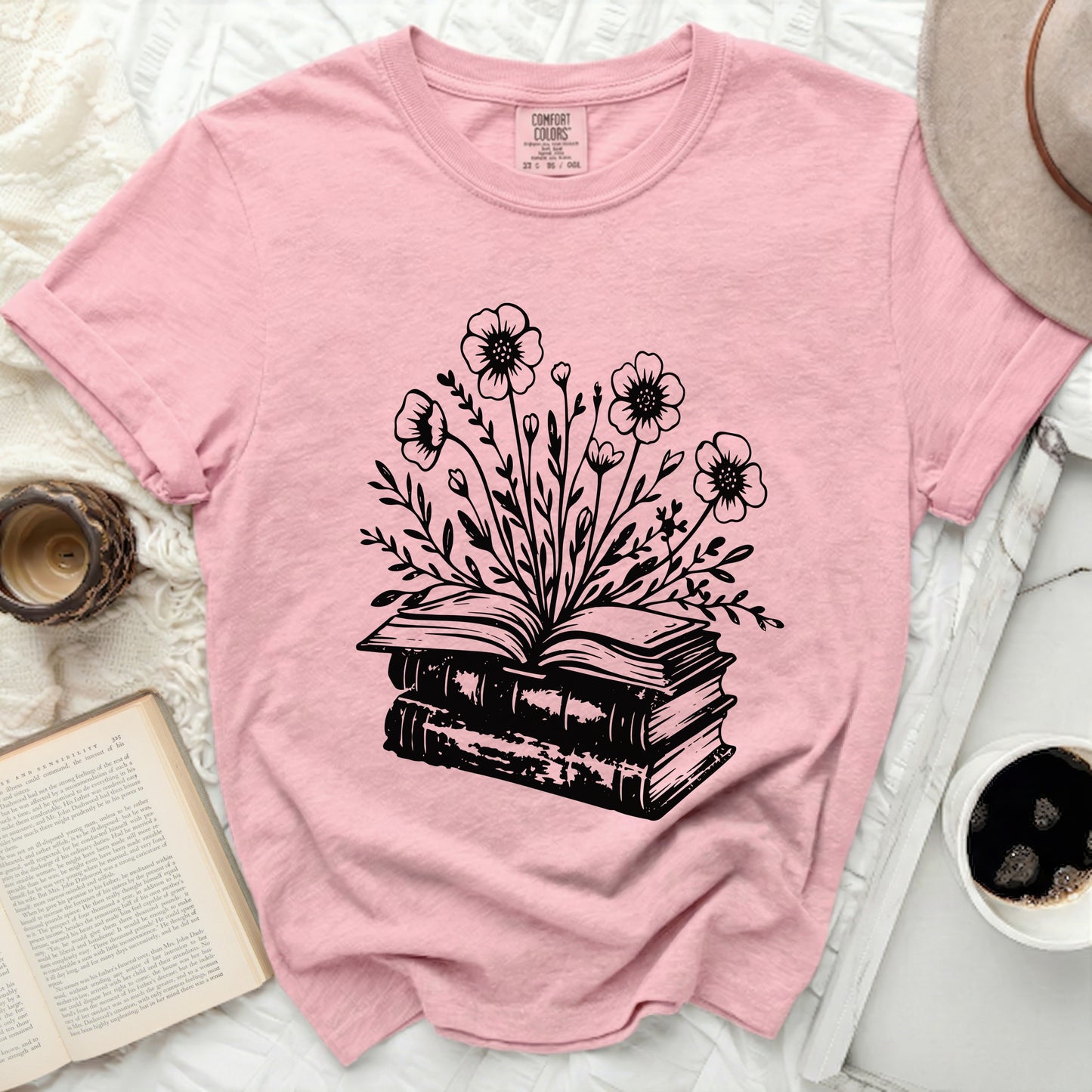 Pink t-shirt with black floral design emerging from open books.