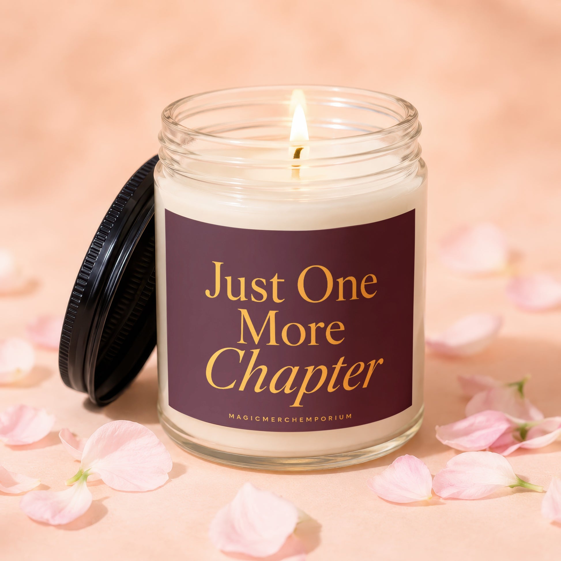 Glass candle with lit wick and "Just One More Chapter" text on label.