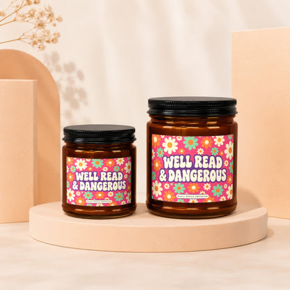 Two amber glass candles with floral labels reading "Well Read & Dangerous."