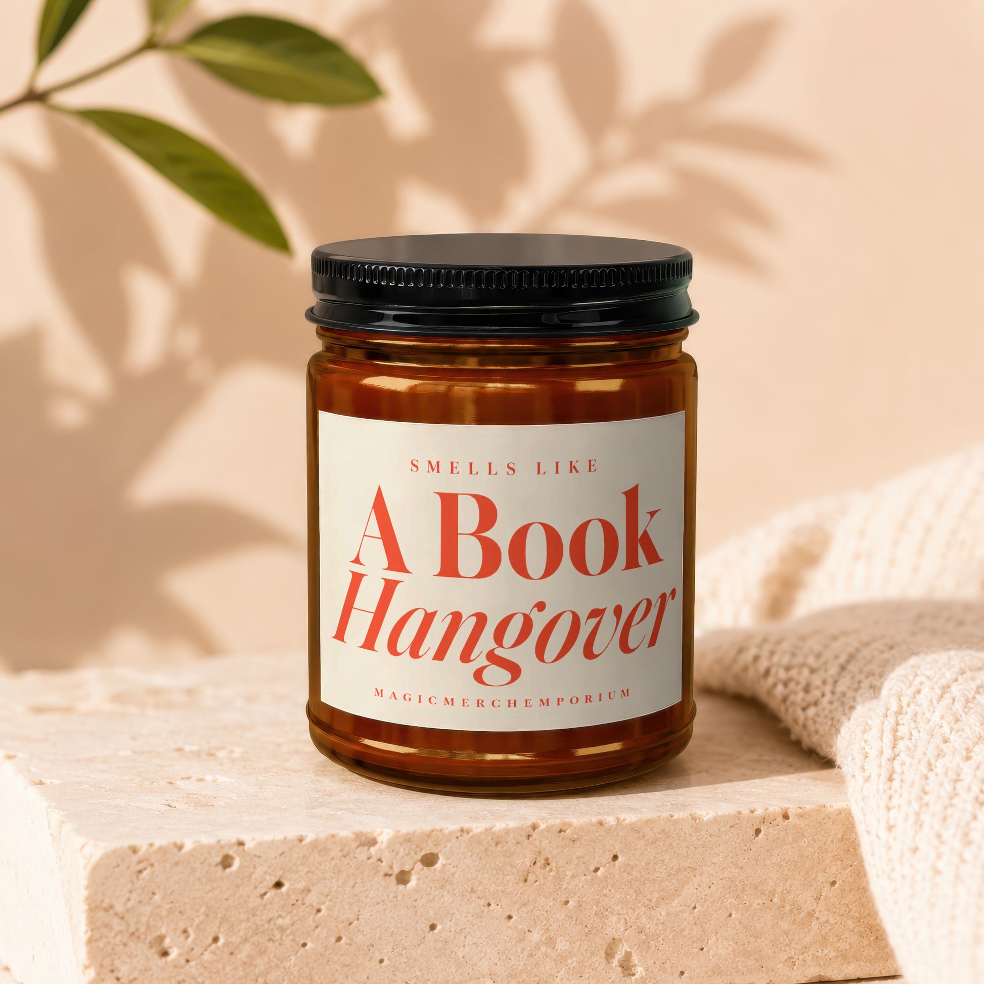 Candle in amber jar with black lid, reads "A Book Hangover" and "MagicMerchEmporium".