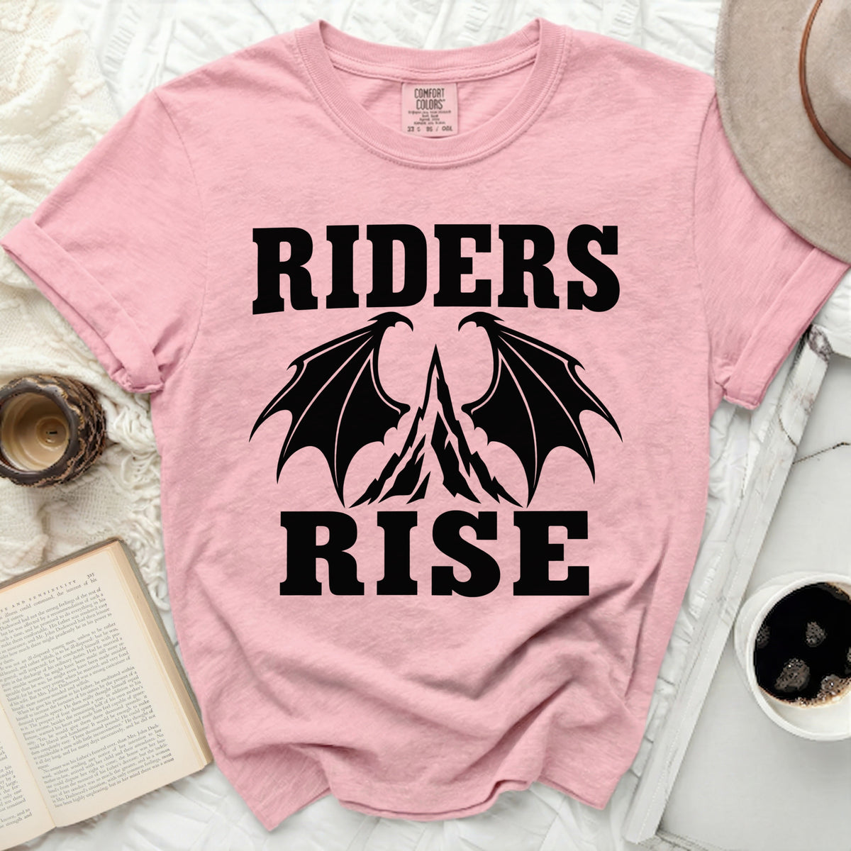 Pink t-shirt with black text and dragon wings graphic reading "RIDERS RISE"
