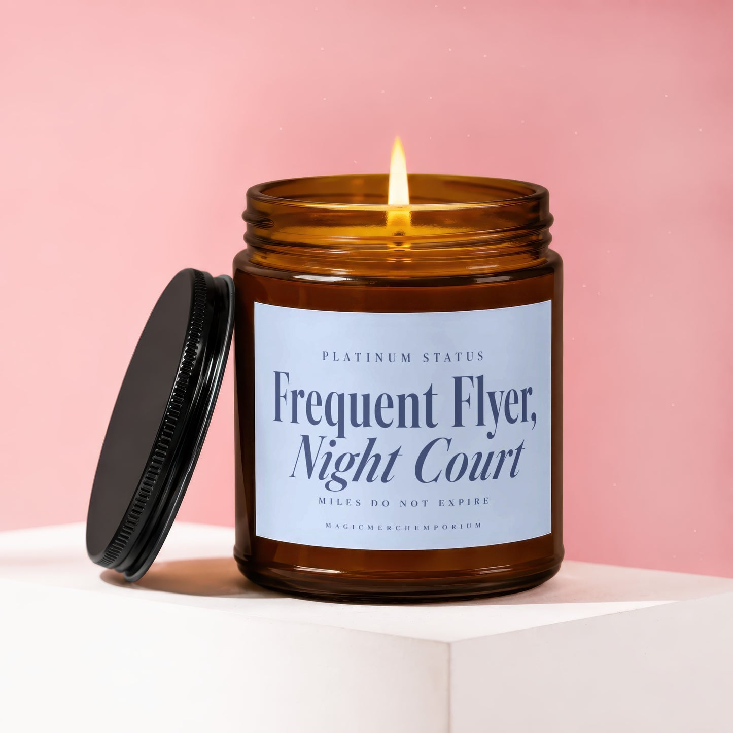 Amber glass candle with lit flame, black lid askew, text "Frequent Flyer, Night Court".