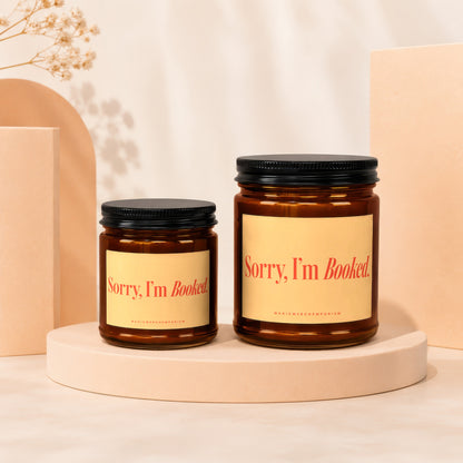 Two amber glass candles with black lids and yellow labels reading "Sorry, I'm Booked."