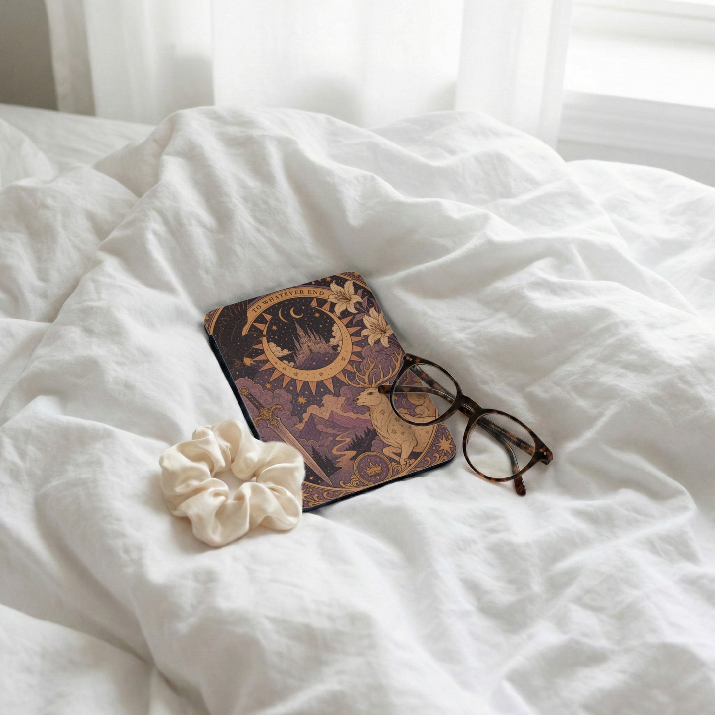 Journal with celestial art, glasses, and scrunchie on rumpled white sheets.