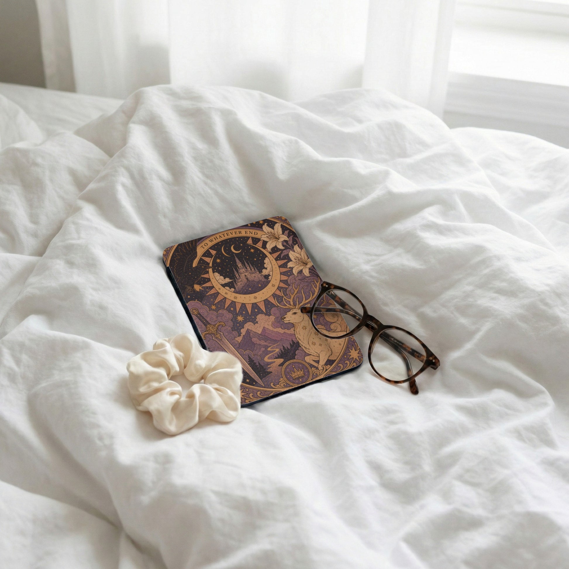 Journal with celestial art, glasses, and scrunchie on rumpled white sheets.