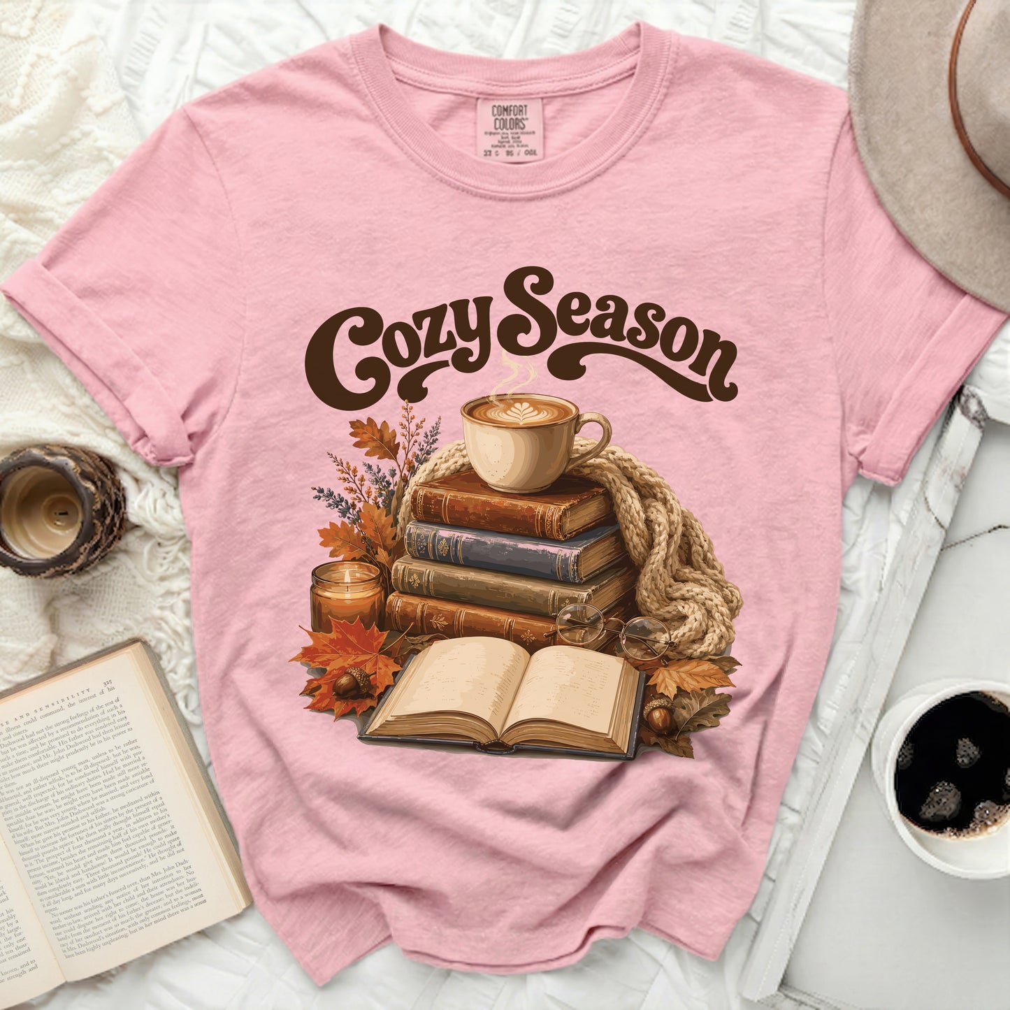 Pink t-shirt with "Cozy Season" graphic featuring coffee, books, and autumn leaves.