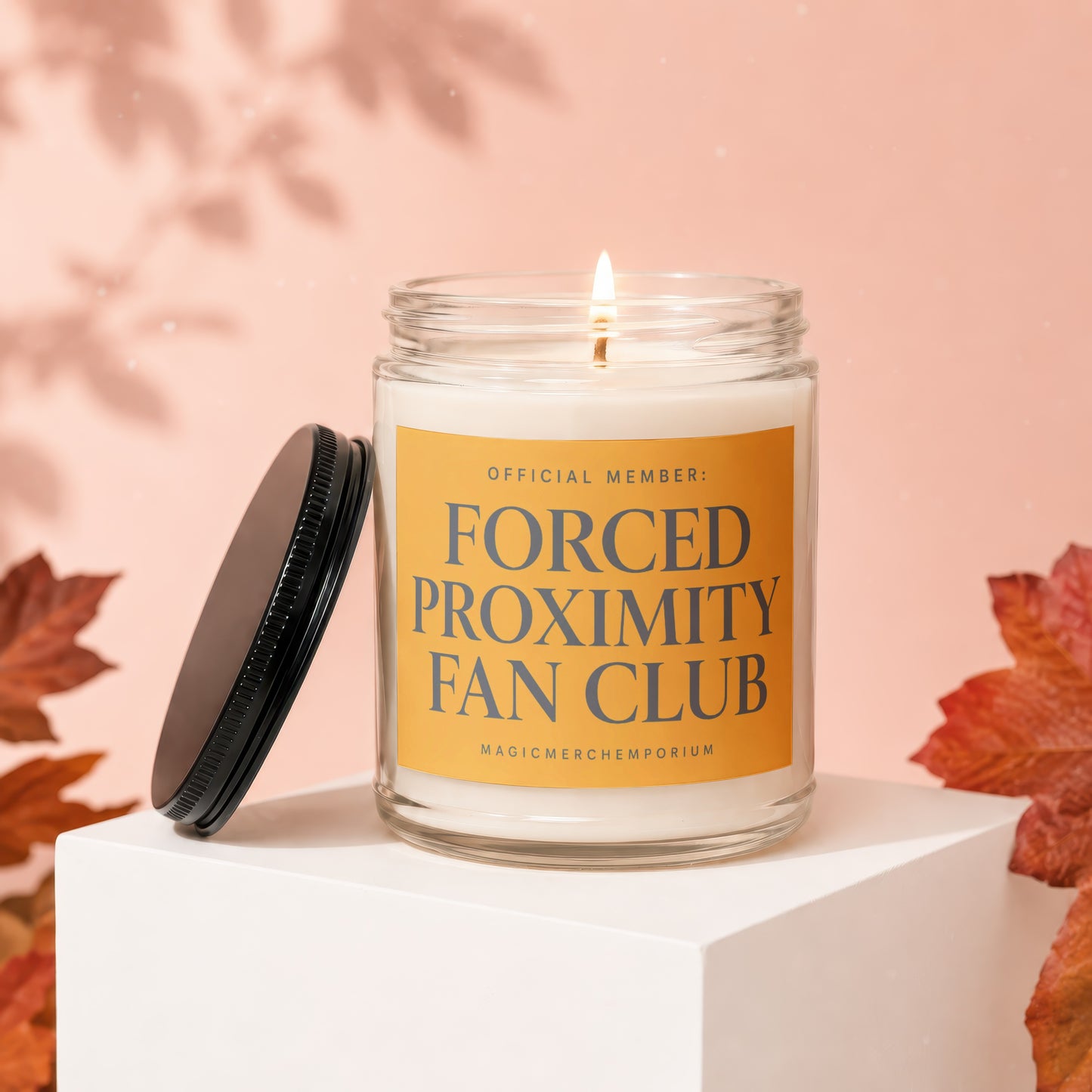 Glass candle with lit wick and an orange label reading "Official Member: Forced Proximity Fan Club".