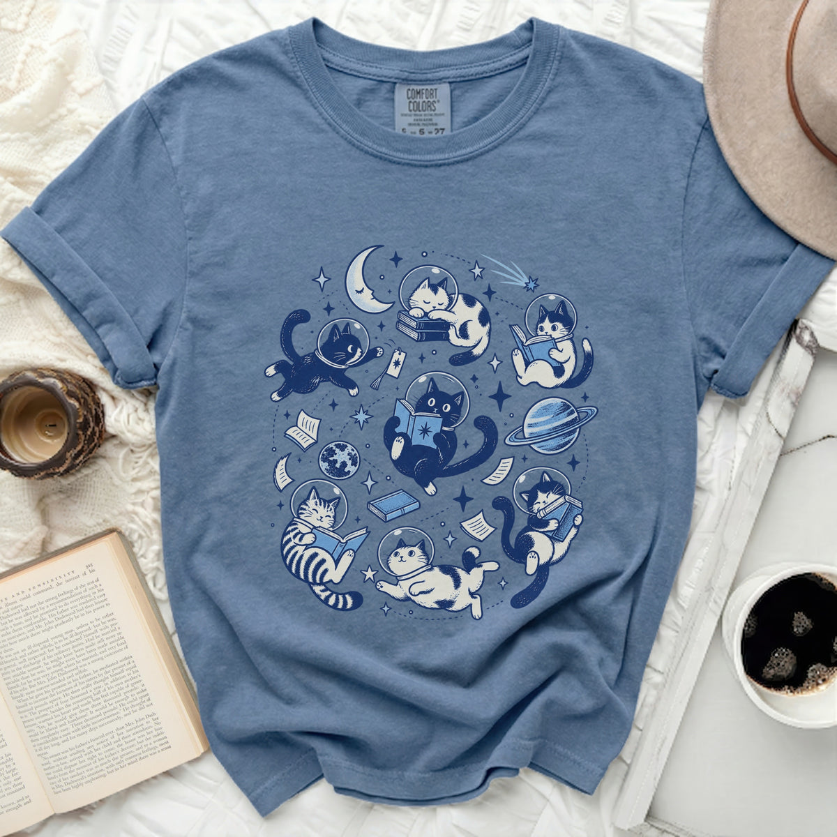 Blue t-shirt with space cats reading books around a crescent moon.
