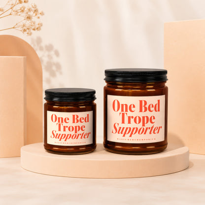 Two amber glass candles, one larger than the other, with "One Bed Trope Supporter" text.