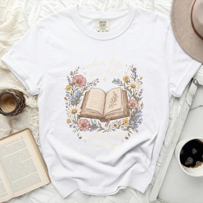 White t-shirt with floral wreath and open book graphic.