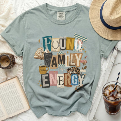 Green t-shirt with "Found Family Energy" text collage and sleeping cat graphic.