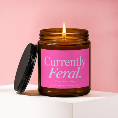 Amber jar candle lit with pink label reading "Currently Feral. it's a book thing."