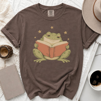 Brown t-shirt with graphic of a smiling frog reading a book surrounded by stars.