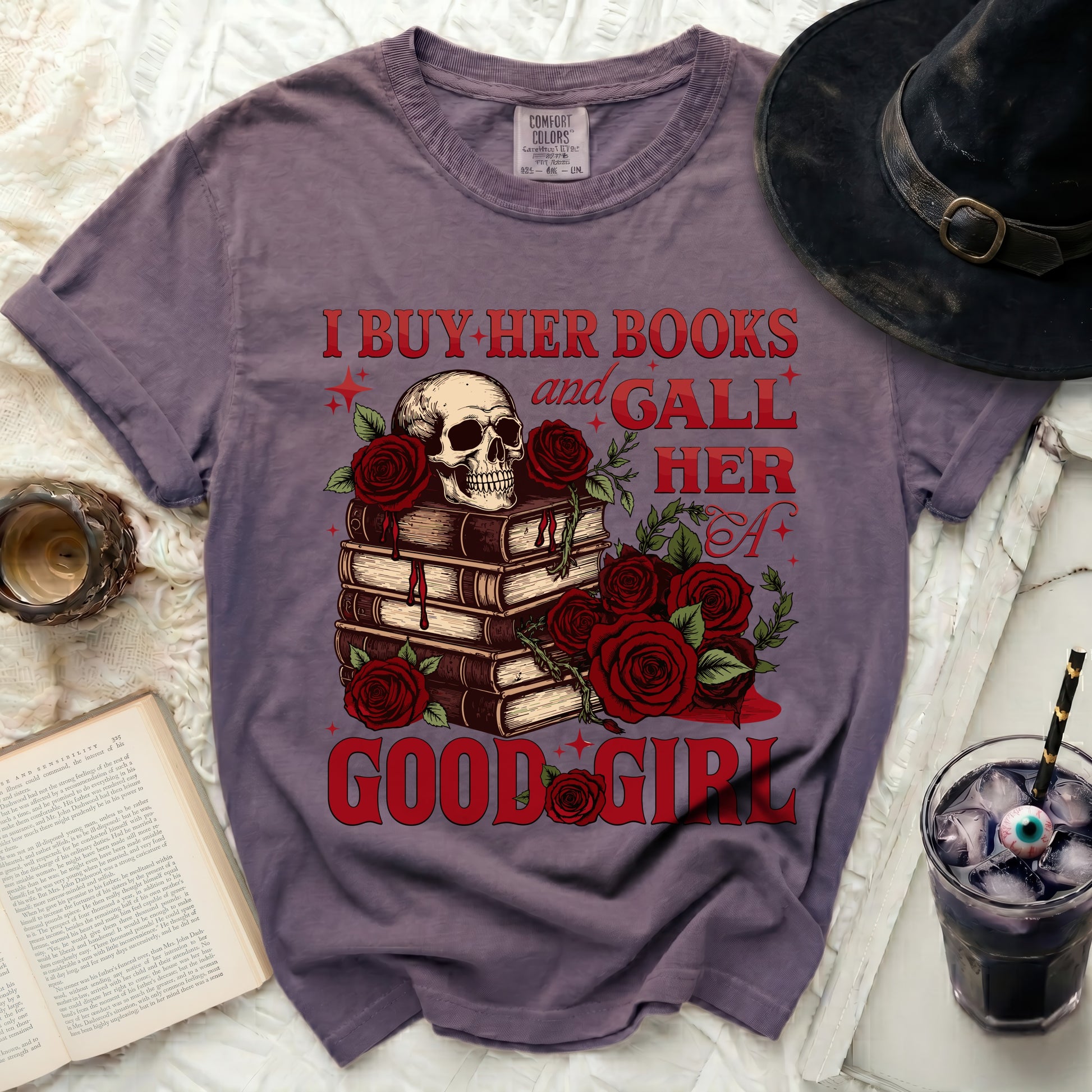 Purple t-shirt with skull, books, and roses graphic reading "I buy her books and gall her a good girl".