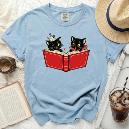 Light blue t-shirt with cartoon black cats reading a red book.