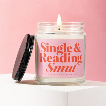 Glass candle with pink label reading "Single & Reading Smut" on pink background.