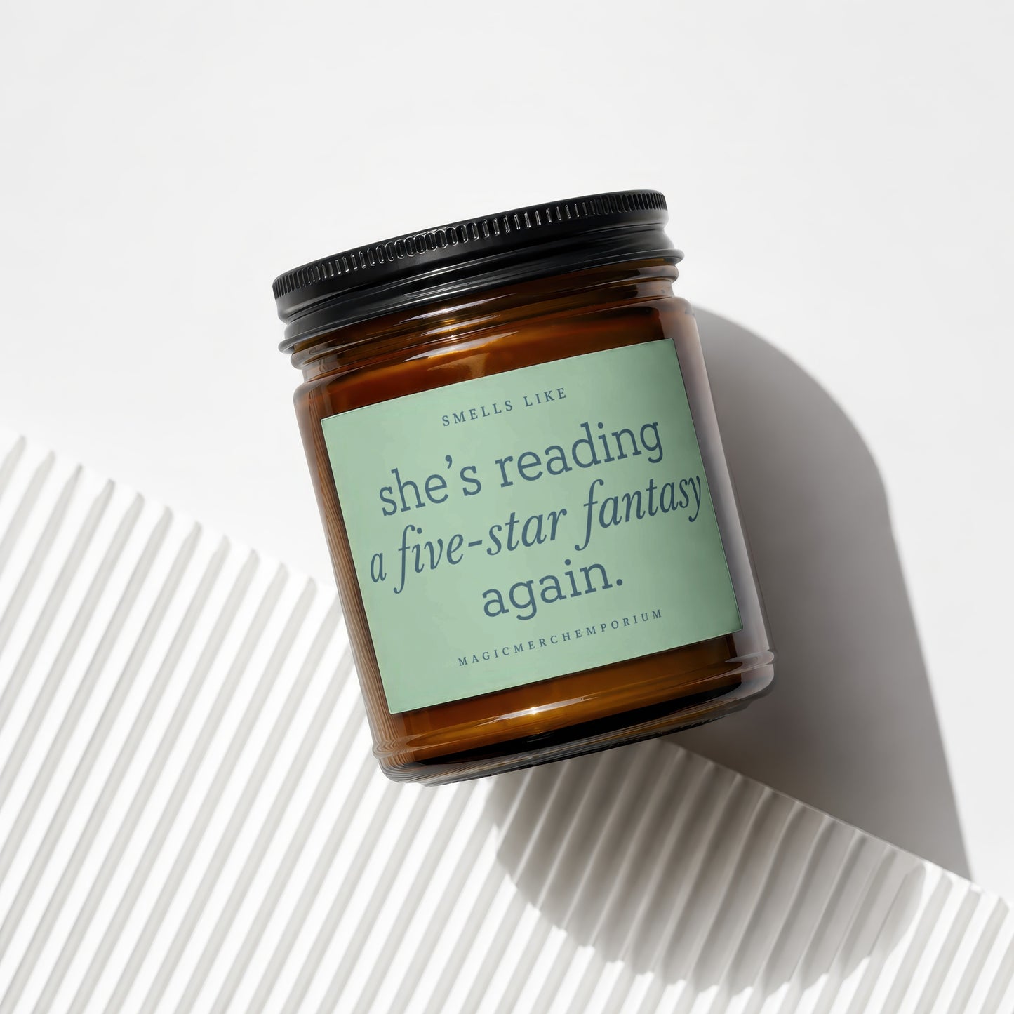 Brown glass candle with a light green label reading "smells like she's reading a five-star fantasy again."