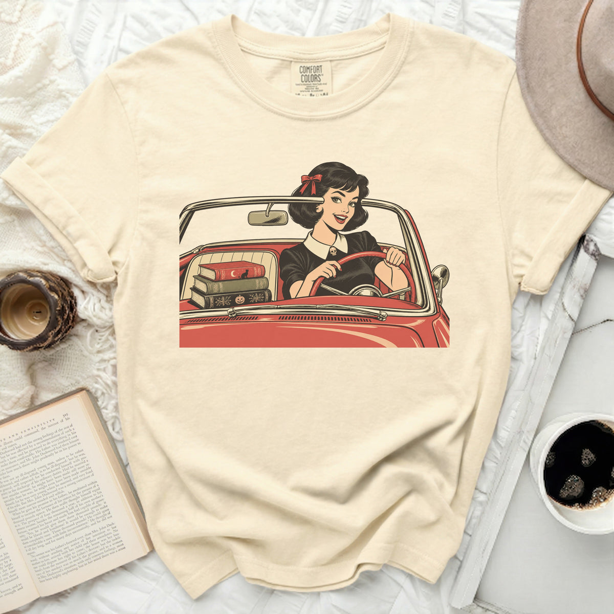 Cream t-shirt with graphic of woman driving red car, carrying books.