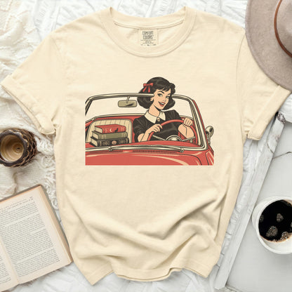 Cream t-shirt with graphic of woman driving red car, carrying books.