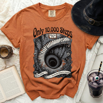 Orange t-shirt with graphic of spiral stairs, text "Only 10,000 Steps" and "Mind the Drop".