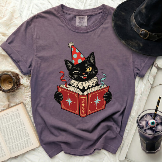 Black cat wearing party hat reads a red book with star designs.