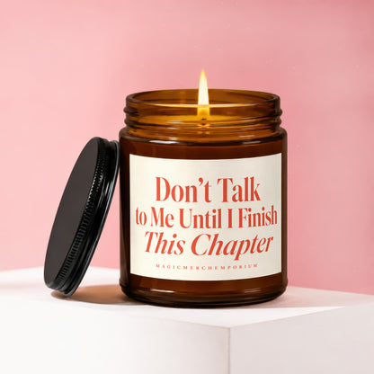 Amber glass candle with lit flame and black lid. Label reads "Don't Talk to Me Until I Finish This Chapter".