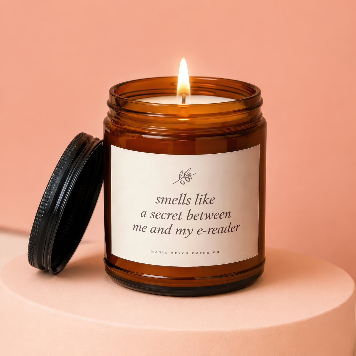 Amber jar candle with lit wick, reading "smells like a secret between me and my e-reader."