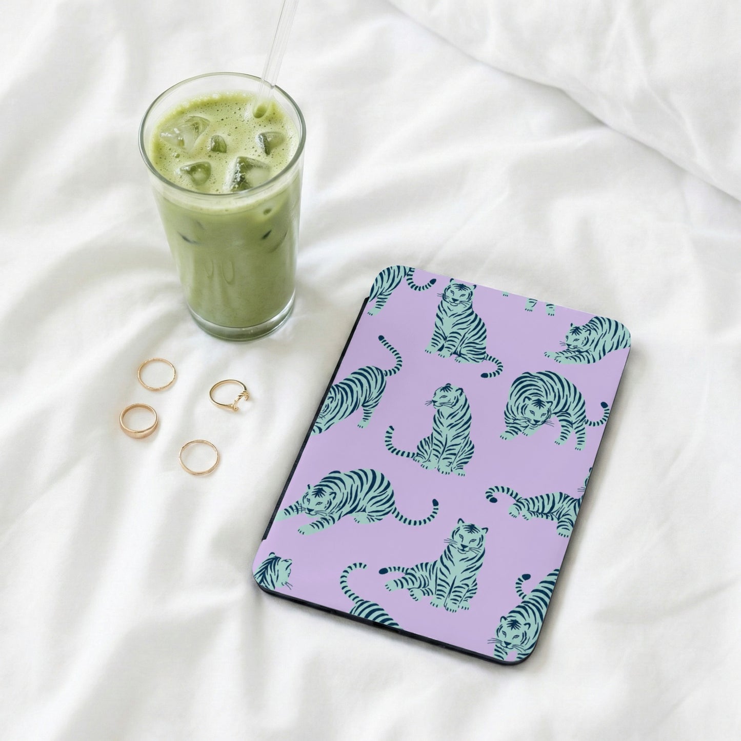 Lavender case with teal tigers, next to iced matcha drink and gold rings.