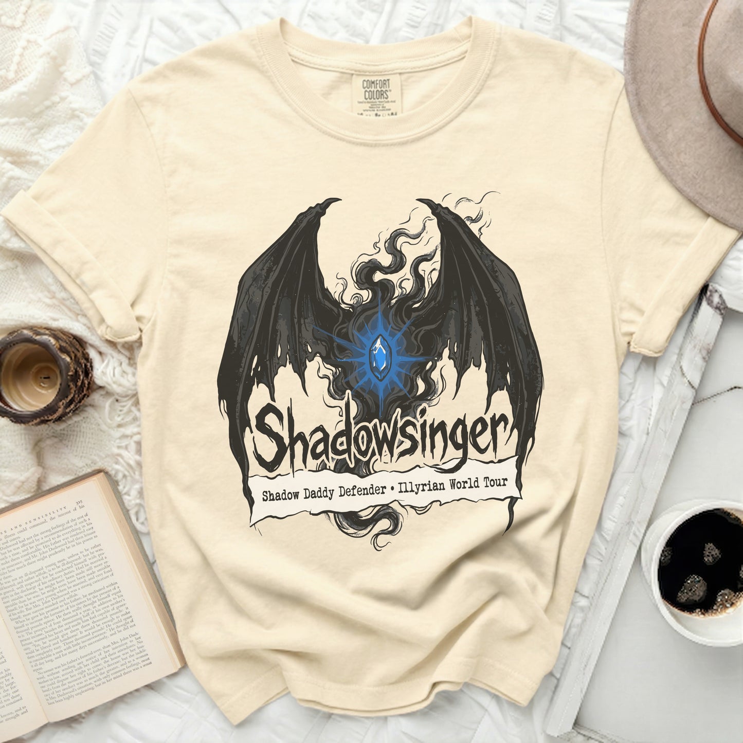 Cream t-shirt with black wings and blue gem, "Shadowsinger" text.
