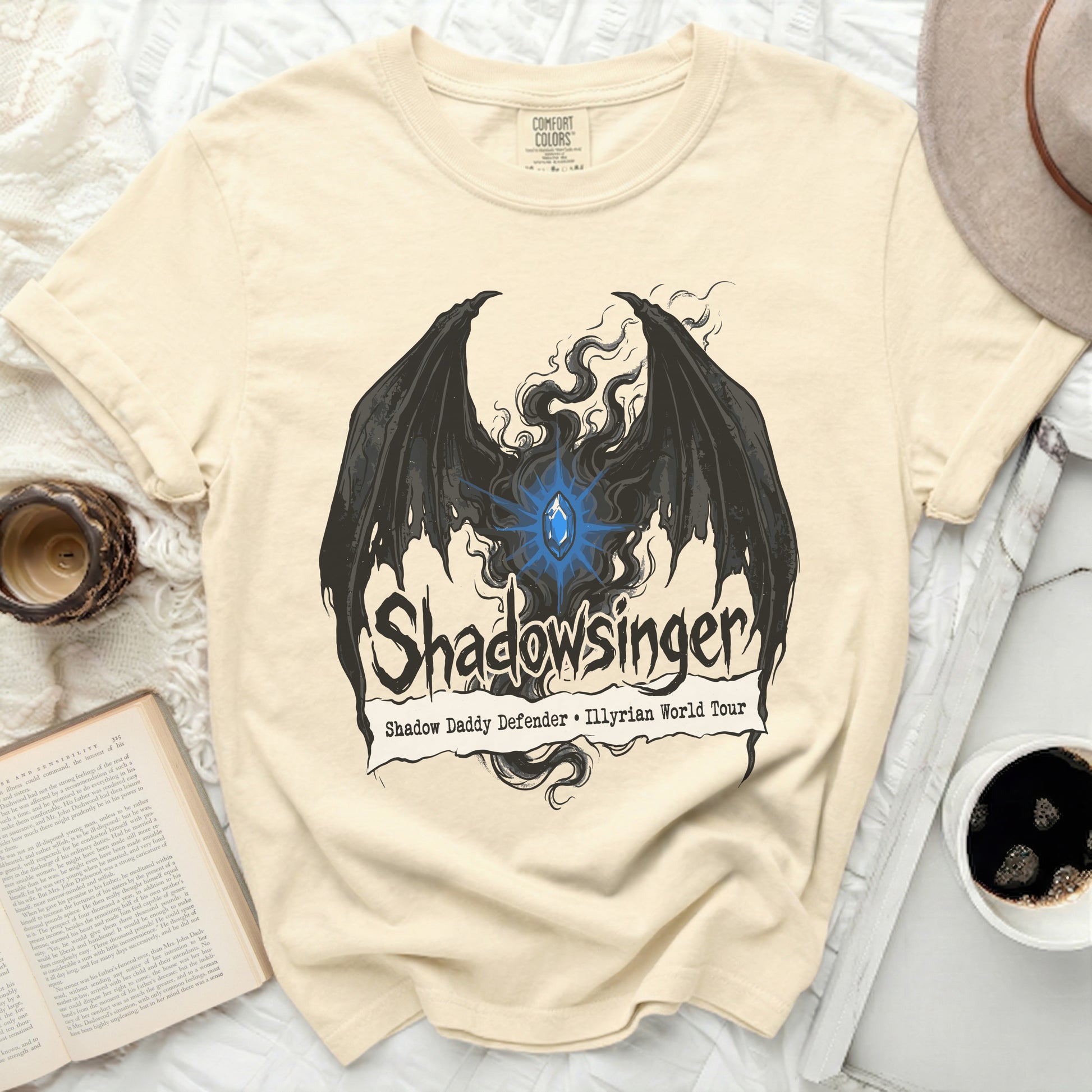 Cream t-shirt with black wings and blue gem, "Shadowsinger" text.