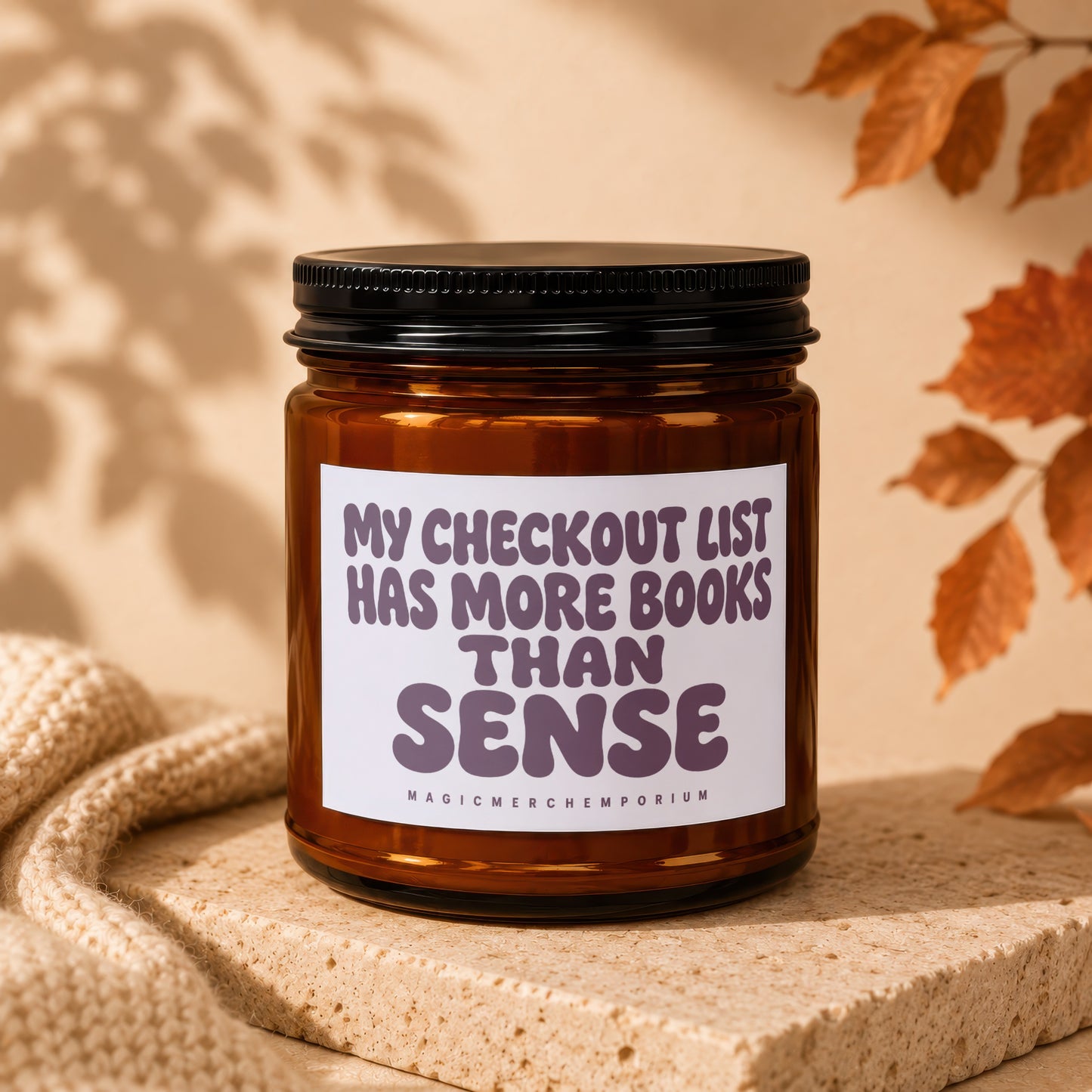 Amber jar candle with black lid reading "MY CHECKOUT LIST HAS MORE BOOKS THAN SENSE".