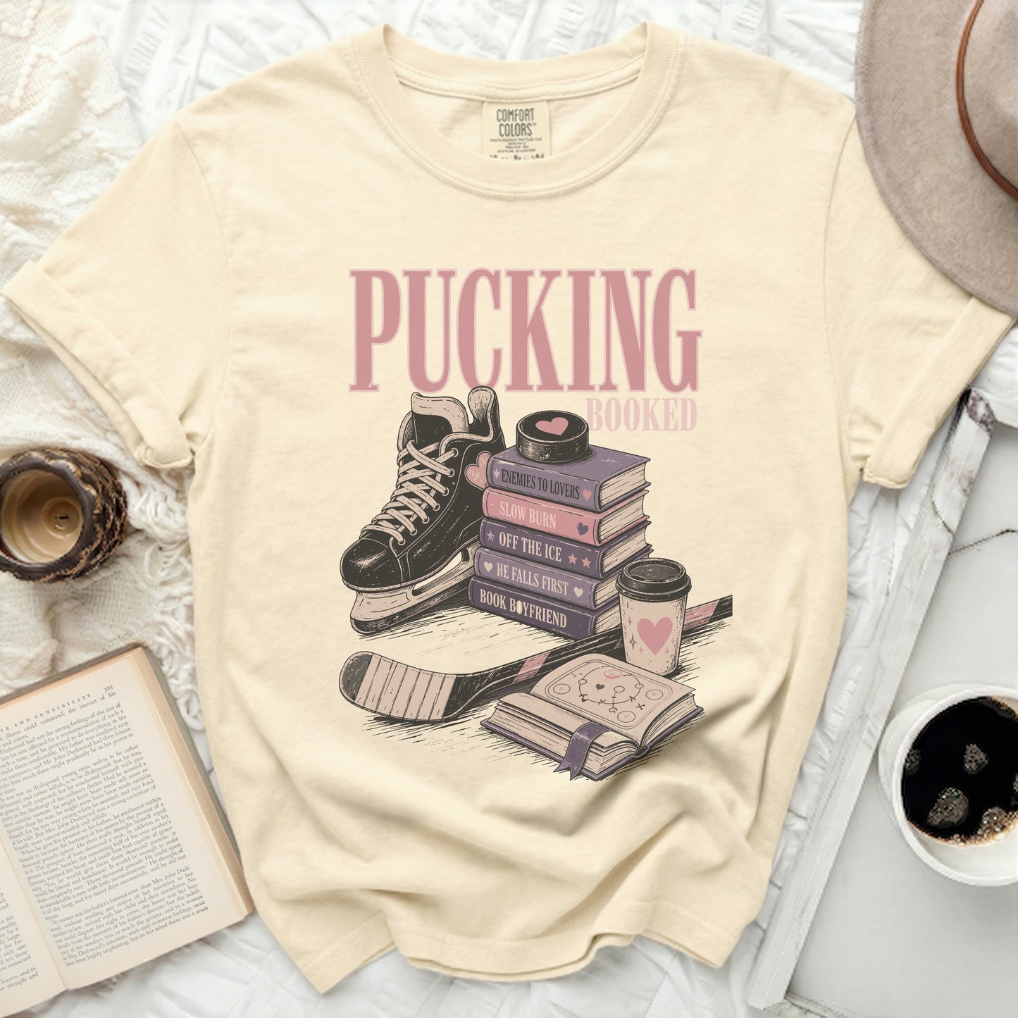 Cream t-shirt with "Pucking Booked" and stacked books with ice skate.