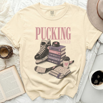 Cream t-shirt with "Pucking Booked" and stacked books with ice skate.