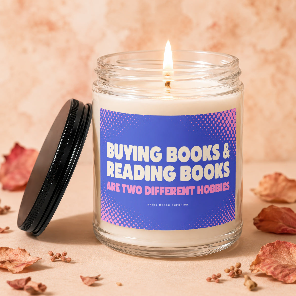 Lit candle in glass jar with blue label reading "Buying Books & Reading Books Are Two Different Hobbies".