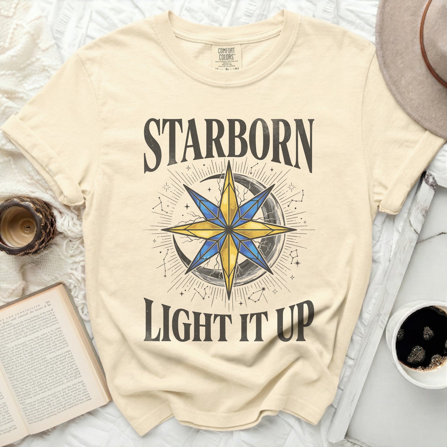 Cream t-shirt with "STARBORN LIGHT IT UP" text and celestial graphic.