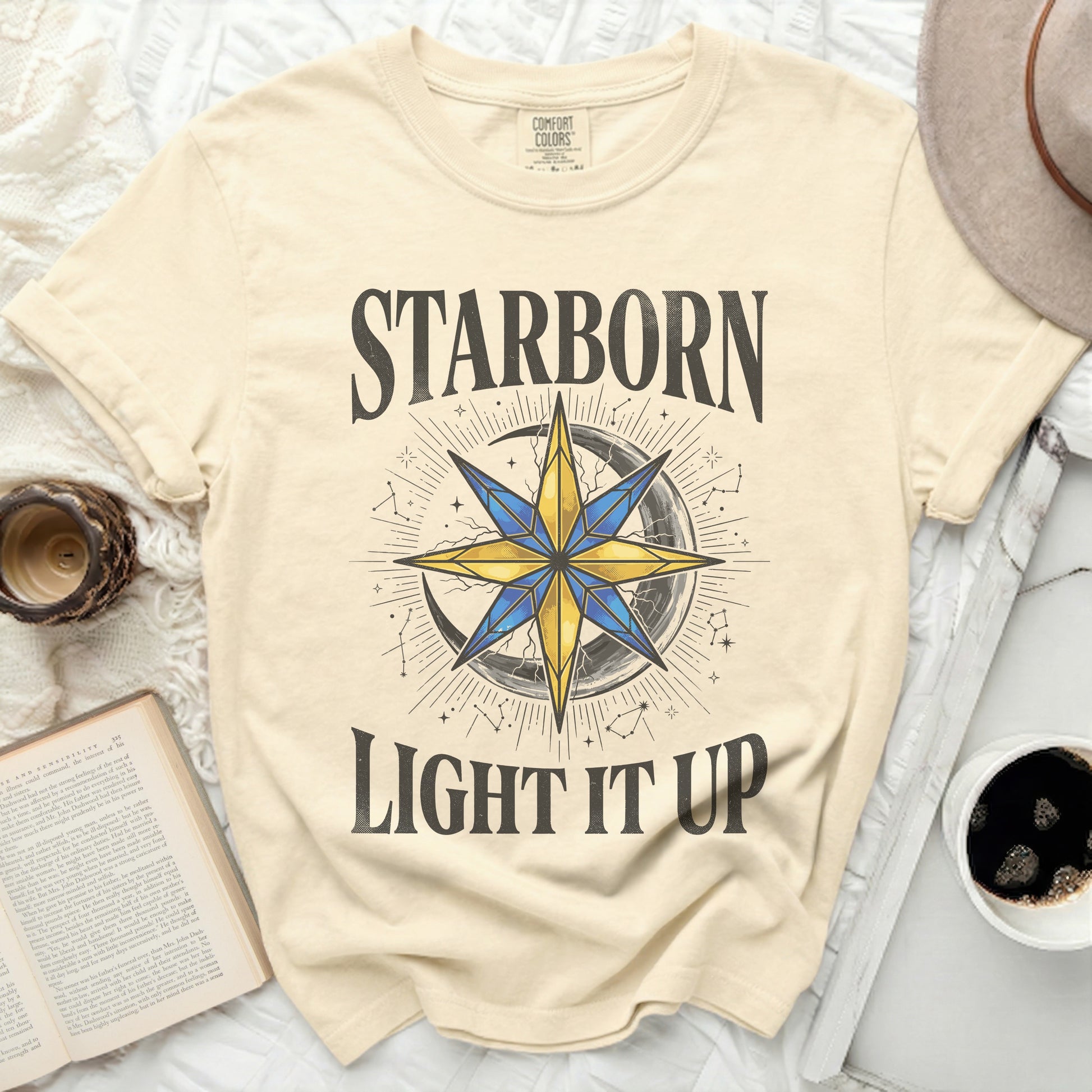 Cream t-shirt with "STARBORN LIGHT IT UP" text and celestial graphic.