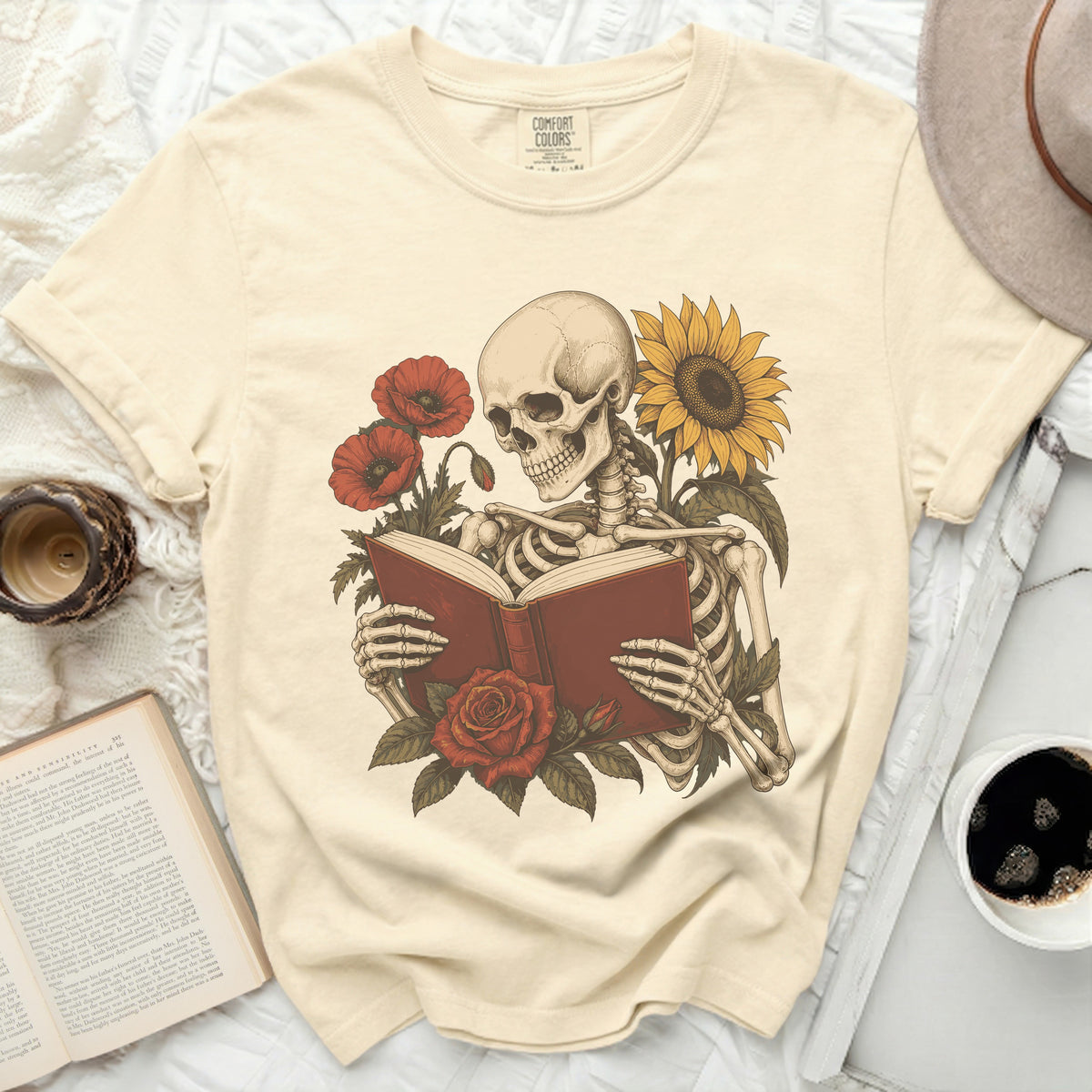 Skeleton reading a book surrounded by poppies and a sunflower.