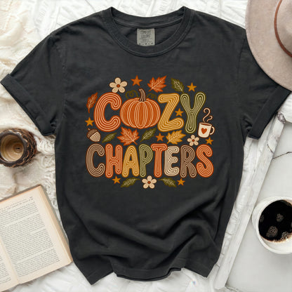 Dark grey t-shirt with "COZY CHAPTERS" text, pumpkin, leaves, and coffee mug graphic.