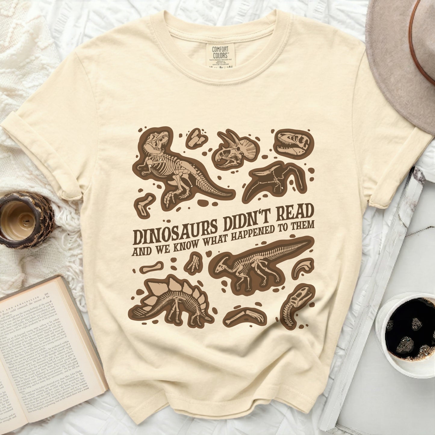 Cream t-shirt with brown dinosaur skeletons and text: "Dinosaurs Didn't Read And We Know What Happened To Them".